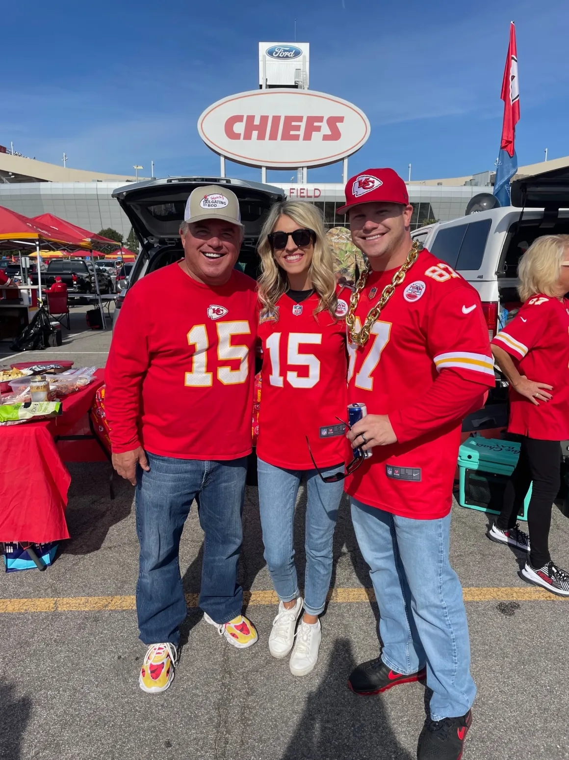 Three people in Chiefs jerseys tailgating.